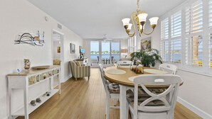 A spacious dining area with a round table, white chairs, and a view of the sea through large windows.