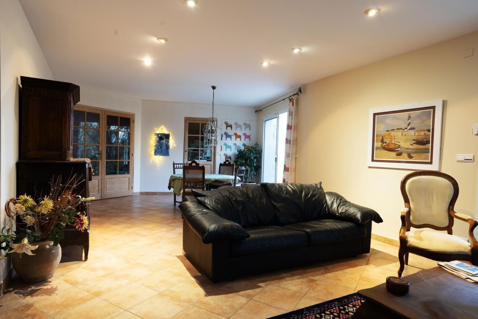 A spacious living room with a black leather sofa, a wooden chair, and a dining area with a table and chairs.