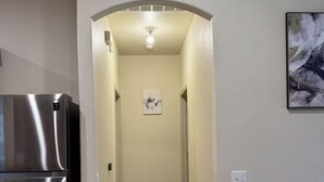 A hallway with a stainless steel refrigerator on the left, a carpeted floor, and a painting on the right wall.