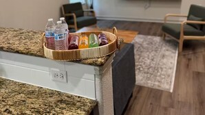 A living room with a television, a ceiling fan, and a basket of bottled water on a counter.