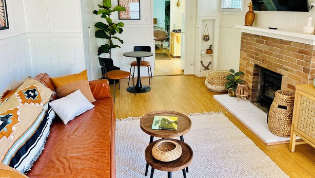 A living room with a sofa, a coffee table, a fireplace, and a television mounted on the wall. - Breezy Bayside Escape — Cottage with Patio in Heart of Mission Beach (San Diego)