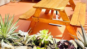 A wooden picnic table with a bench, an umbrella, and potted plants. - Breezy Bayside Escape — Cottage with Patio in Heart of Mission Beach (San Diego)