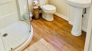 A bathroom with a glass shower enclosure, a toilet, a sink, and a window. - Breezy Bayside Escape — Cottage with Patio in Heart of Mission Beach (San Diego)