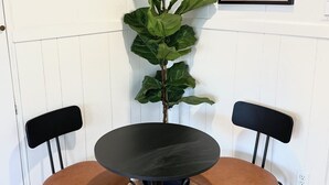 A room with a round black table and two brown chairs, a potted plant, and a framed artwork on the wall. - Breezy Bayside Escape — Cottage with Patio in Heart of Mission Beach (San Diego)
