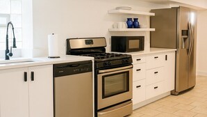 Une cuisine moderne avec des meubles blancs, des appareils électroménagers en acier inoxydable et un sol carrelé.