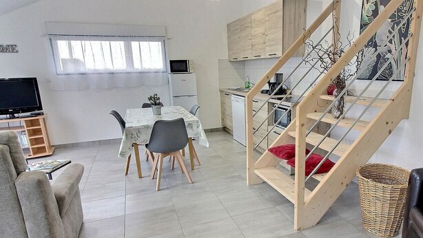 Un espai habitable petit amb zona de menjador, petita cuina i escala de fusta.