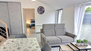 Un saló modern amb un sofà gris, una escala de fusta, una taula de menjador amb un mantell floral i una finestra gran amb cortines.