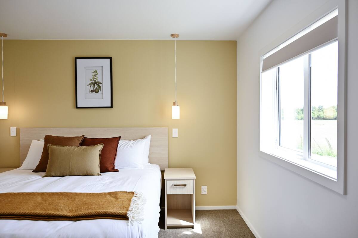 A neatly arranged bedroom with a bed, bedside table, and a large window.