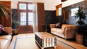 Een woonkamer met een houten salontafel, een leren bank, een kroonluchter en een groot raam met gordijnen.