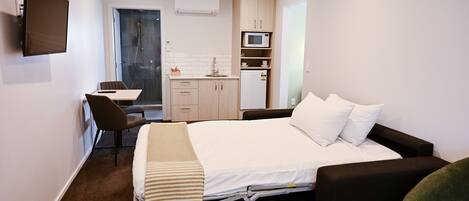 Een compacte hotelkamer met een bed, een bureau met stoel, een kitchenette en een douche.