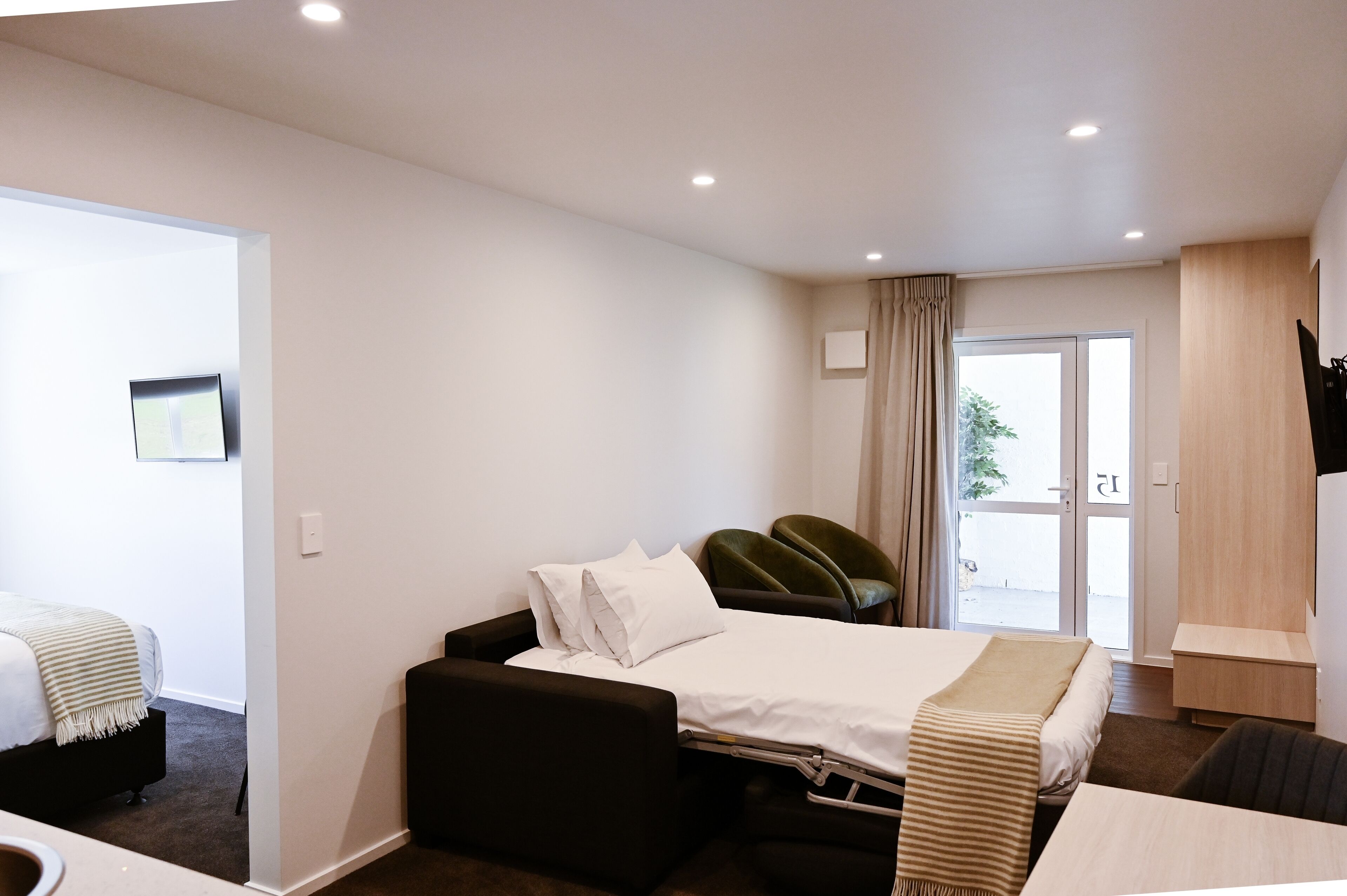 A hotel room with a bed, a desk, a chair, a TV, and a sliding door to the outside.
