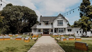 Een wit huis met twee verdiepingen, een voortuin met buitenmeubilair en lichtslingers.