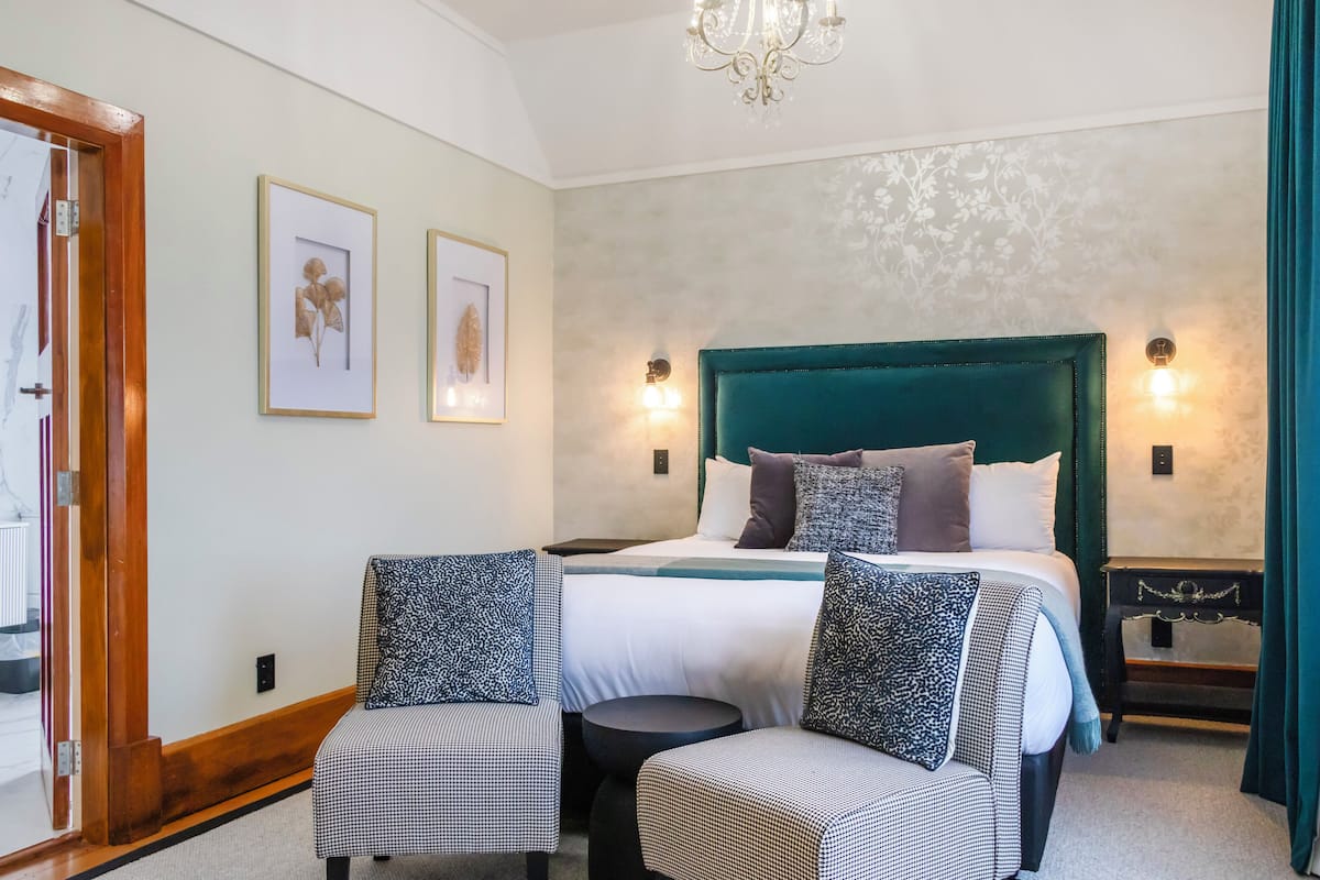 A bedroom with a large bed, two chairs, a nightstand, and a chandelier.