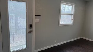 Una habitación con una puerta, dos ventanas y un suelo de madera oscura.