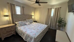 Un dormitorio con una cama, mesitas de noche, un ventilador de techo y una planta en maceta.