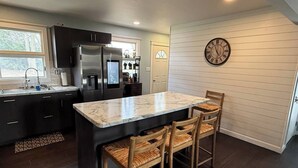 Una cocina moderna con armarios oscuros, una isla de mármol y una zona de comedor de madera.