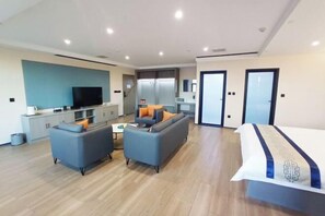 A modern hotel room with a sofa, a TV, a bed, and a kitchenette. - Tianma Hotel (Hami)