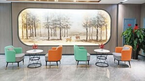 Un hall d’entrée agrémenté d’une grande fresque représentant une scène de forêt, de quatre chaises colorées et d’une plante en pot.