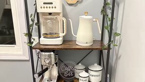 Una estación de café con cafetera, hervidor y varios artículos relacionados con el café sobre un estante de madera.