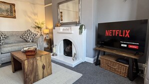 Una sala de estar con chimenea, un sofá, una mesa de centro y un televisor que muestra el logotipo de Netflix.