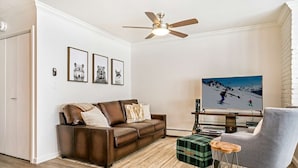 A living room with a brown leather sofa, a grey armchair, a television, and framed pictures on the wall.