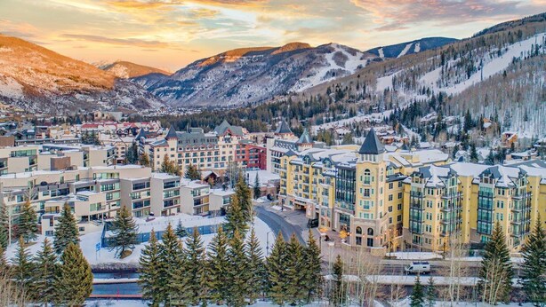 A snow-covered town with multi-story buildings, including a hotel with a ski lift visible in the background.