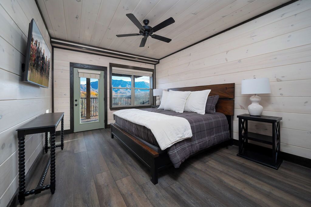 A bedroom with a bed, a nightstand, a ceiling fan, a door leading to a balcony, and a painting on the wall.