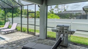 Ein überdachter Außenbereich mit Grill, Liegestühlen und Blick auf eine Straße sowie Grünflächen.