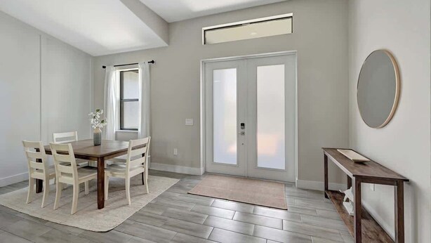 Ein modernes Wohnzimmer mit einem Holzesstisch, weißen Stühlen, einem großen Fenster und einer Tür mit Milchglas-Fenstern.