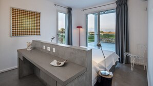 Ein modernes Schlafzimmer mit einer Betonbank, einem Bett, einem großen Fenster und Blick ins Freie.