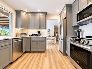 A modern kitchen with grey cabinets, stainless steel appliances, and a wooden floor.