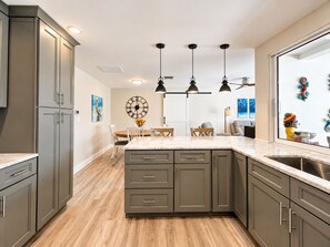 A modern kitchen with grey cabinets, a marble countertop, and pendant lighting.