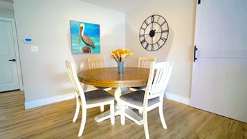Un coin repas avec une table en bois, des chaises blanches, une horloge et un tableau représentant un oiseau.