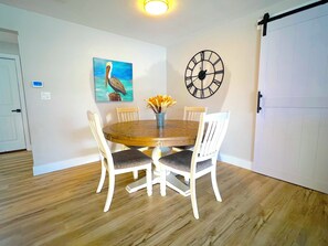 Een eetruimte met een houten tafel, witte stoelen, een klok en een schilderij van een vogel.