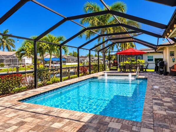 A swimming pool with a covered area, surrounded by palm trees and a clear blue sky.