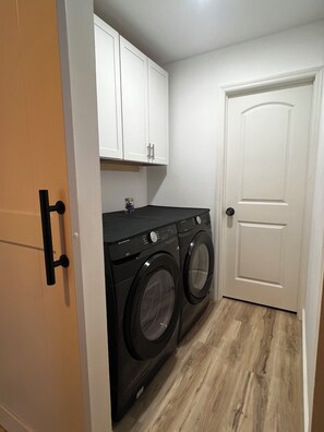 Een wasserij met een wasmachine en droger, houten kastjes en een witte deur.
