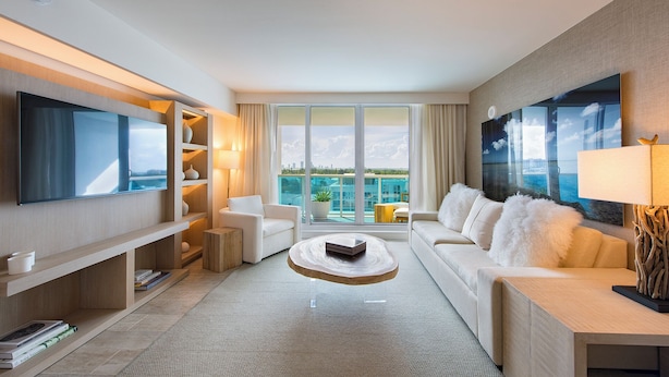 Una moderna camera d'hotel con una grande televisione a schermo piatto, un divano, un tavolino da caffè e vista sull'oceano attraverso ampie finestre.