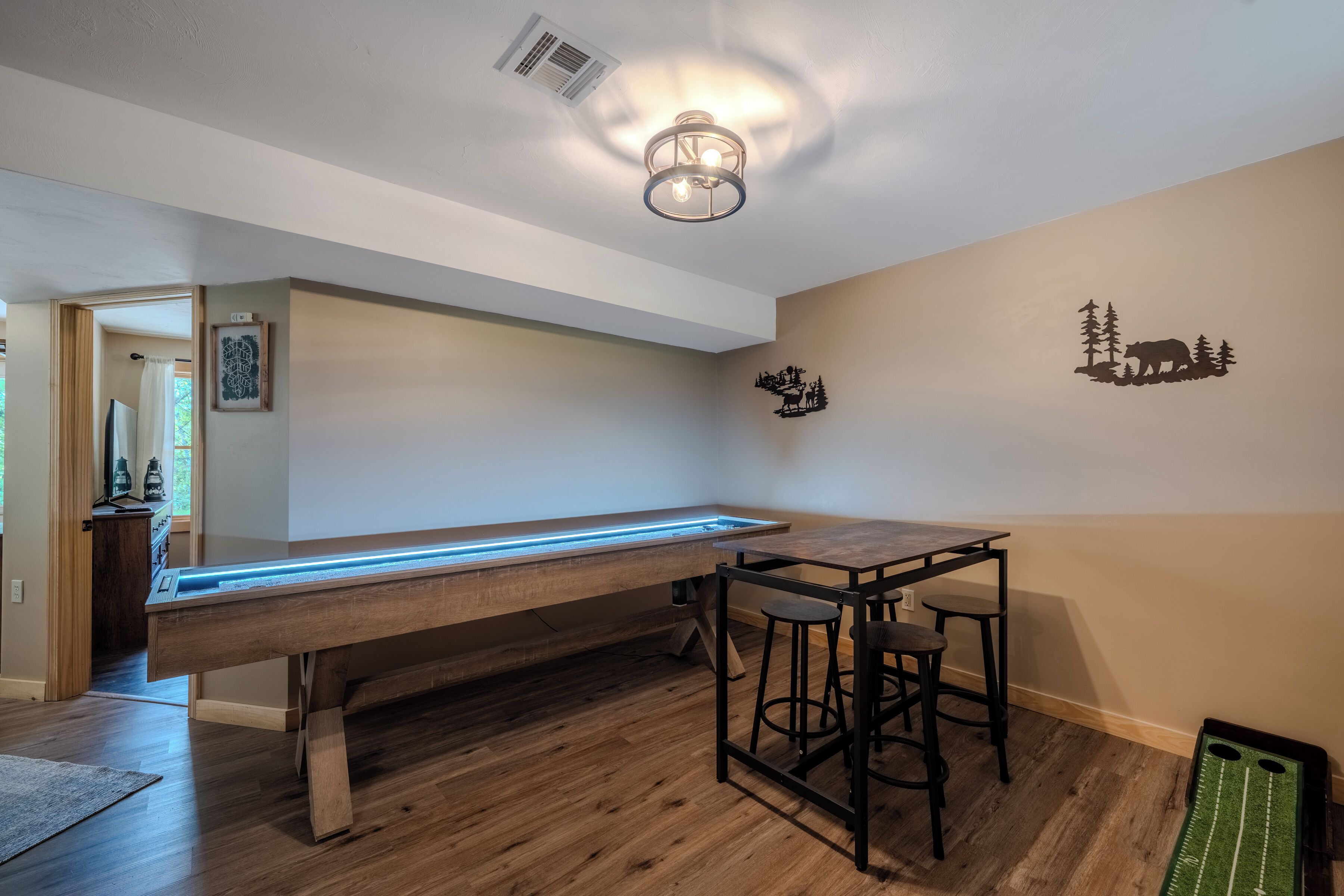 A pool table with a neon light, a bar stool, and a wall decal of a bear and trees.