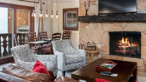 A cozy living room with a fireplace, patterned chairs, a sofa, and a television mounted on the wall. - Modern 2 Bedroom Condo at the Base of Vail Mountain Next to Gondola One (Vail)