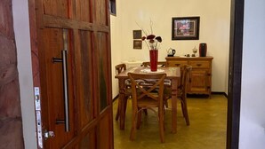 Un coin repas avec une table et des chaises en bois, un lustre et un buffet en bois orné d’un vase de fleurs.