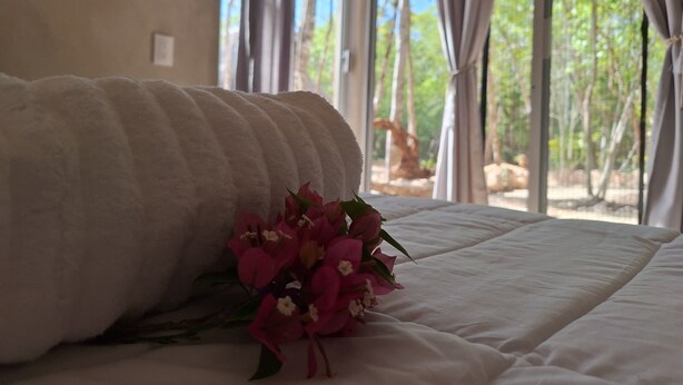 Un lit avec une couette blanche et un bouquet de fleurs roses.