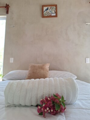 Una cama bien tendida con ropa blanca y una única almohada marrón.