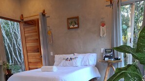 Une chambre avec un lit en bois, une petite table sur laquelle est posé un catalogue et une plante en pot.
