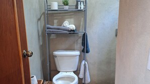 Une petite salle de bain avec des toilettes, une étagère contenant des articles de toilette et une serviette accrochée au mur.