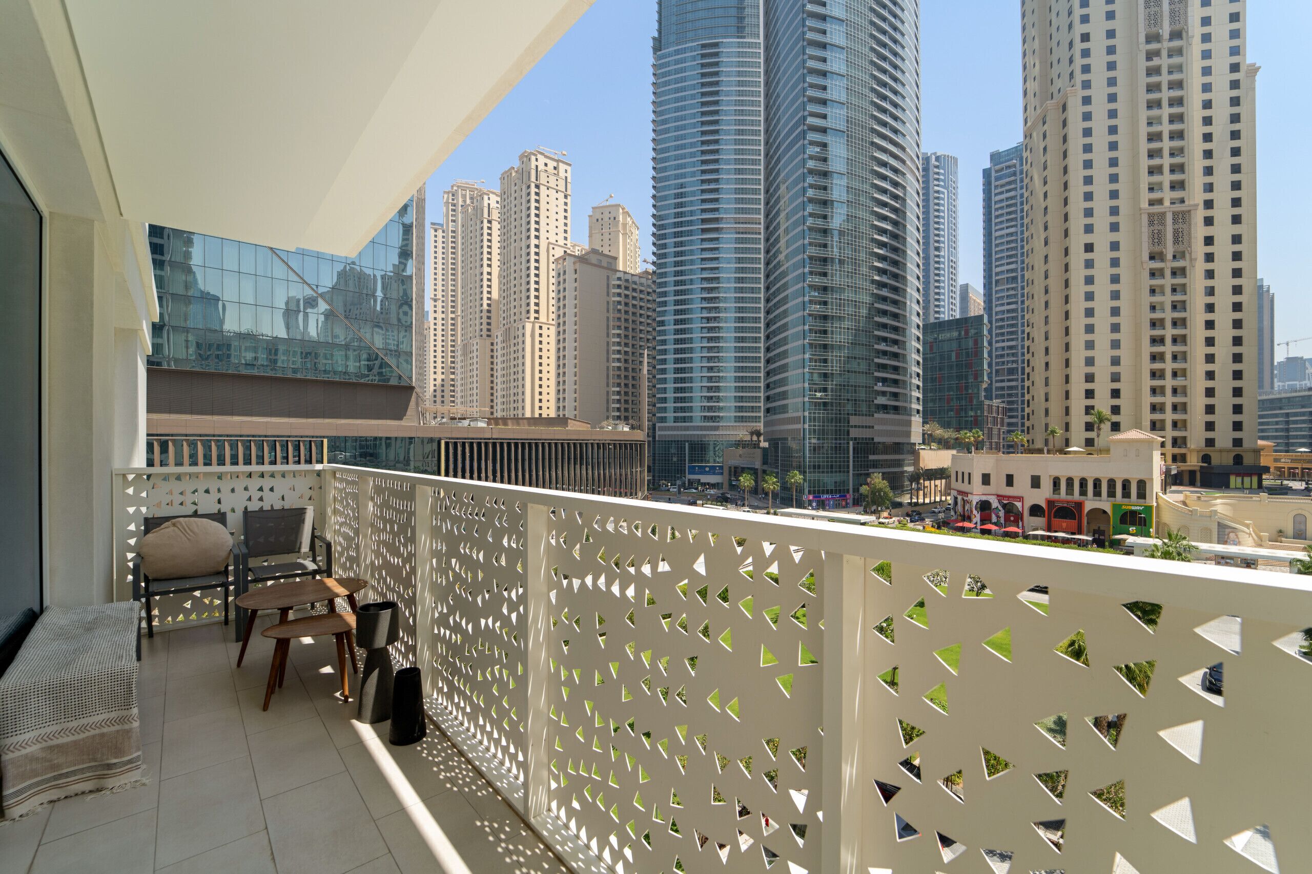 A balcony with a view of high-rise buildings, a seating area with a sofa and table, and a decorative white fence.