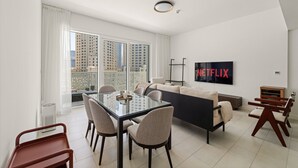 Een moderne woonkamer met een glazen eettafel, banken en een aan de muur bevestigde televisie.