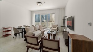 Een moderne woonkamer met een bank, fauteuils, een salontafel, een televisie en een balkon met uitzicht op de stad.