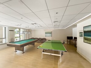 A room with a pool table, ping pong table, and seating area.