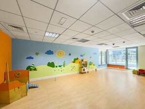 A spacious room with a wooden floor, a large window with a view of greenery, and a colorful mural on the wall.