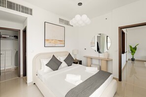 A modern hotel room with a large bed, a bedside table with a lamp, a round mirror, and a potted plant.